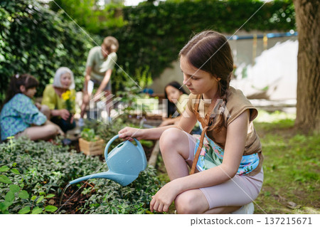 Portrait of cute schoolgirl taking care of plants in school garden during at outdoor sustainable education class. Concept of experiential learning and ecoliteracy. 137215671