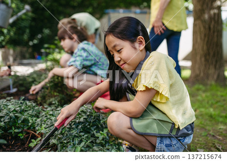 Portrait of cute schoolgirl taking care of plants in school garden during at outdoor sustainable education class. 137215674