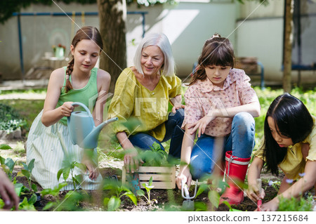 Portrait of students and female teacher at outdoor sustainable education class. Planting vegetable seedling, herbs in soil. 137215684