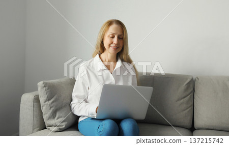Happy modern woman working with laptop, freelancer girl sitting on a couch in the living room 137215742