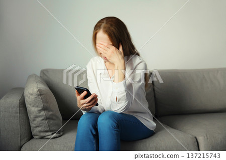 Sad upset crying woman holding phone suffering from stress after reading emotional message at home 137215743