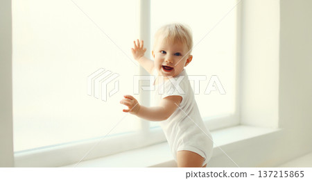 Little baby looking out the window in white room at home 137215865
