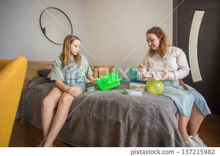 Mom and girl sit on a bed in a small room with pet. 137215982