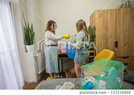 Two individuals work together in a room to clean a pet hamster cage. Two individuals work together in a room to clean a pet hamster cage. 137216008