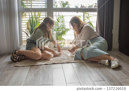 girl and women relax on a rug in a modern indoor space. They share snacks while sitting girl and women relax on a rug in a modern indoor space. They share snacks while sitting 137216010