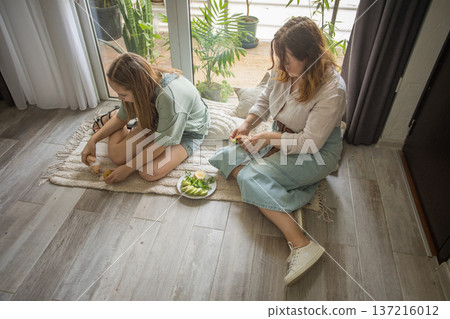girl and women relax on a rug in a modern indoor space. They share snacks while sitting  137216012
