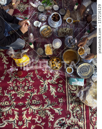 Realistic top view photograph of a traditional Arab family gathering around the table while preparing and sharing iftar during Ramadan. Authentic Ramadan atmosphere, traditional dishes, cultural 137216129