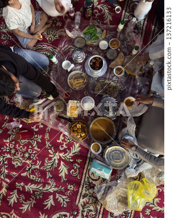 Realistic top view photograph of a traditional Arab family gathering around the table while preparing and sharing iftar during Ramadan. Authentic Ramadan atmosphere, traditional dishes, cultural Realistic top view photograph of a traditional Arab family gathering around the table while preparing and sharing iftar during Ramadan. Authentic Ramadan atmosphere, traditional dishes, cultural 137216133