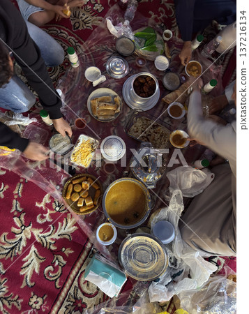 Realistic top view photograph of a traditional Arab family gathering around the table while preparing and sharing iftar during Ramadan. Authentic Ramadan atmosphere, traditional dishes, cultural Realistic top view photograph of a traditional Arab family gathering around the table while preparing and sharing iftar during Ramadan. Authentic Ramadan atmosphere, traditional dishes, cultural 137216134