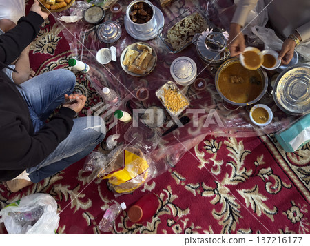 Realistic top view photograph of a traditional Arab family gathering around the table while preparing and sharing iftar during Ramadan. Authentic Ramadan atmosphere, traditional dishes, cultural Realistic top view photograph of a traditional Arab family gathering around the table while preparing and sharing iftar during Ramadan. Authentic Ramadan atmosphere, traditional dishes, cultural 137216177