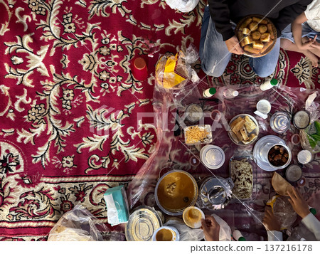 Realistic top view photograph of a traditional Arab family gathering around the table while preparing and sharing iftar during Ramadan. Authentic Ramadan atmosphere, traditional dishes, cultural Realistic top view photograph of a traditional Arab family gathering around the table while preparing and sharing iftar during Ramadan. Authentic Ramadan atmosphere, traditional dishes, cultural 137216178