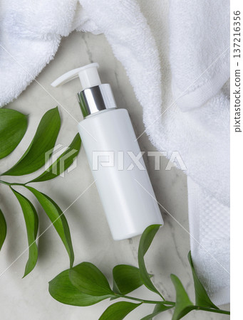 Mockup of blank white pump bottle near white bath terry towel and green leaves. Unbranded cosmetic 137216356