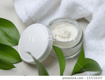 Cosmetic mockup, opened face cream jar with blank lid near white bath towel and green leaves Cosmetic mockup, opened face cream jar with blank lid near white bath towel and green leaves 137216357
