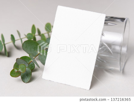 Mockup of blank card near green eucalyptus branche sand crystal glasses. Presentation template 137216365