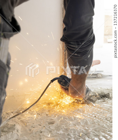 Close up of construction worker using angle grinder to cut wall during renovation, sparks flying Close up of construction worker using angle grinder to cut wall during renovation, sparks flying 137216370