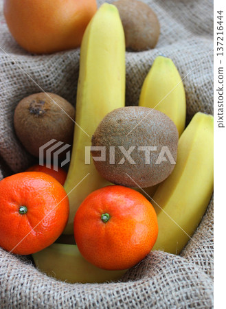 Whole kiwifruits, bananas, mandarins and grapefruit in a fruit basket lined with burlap top view 137216444