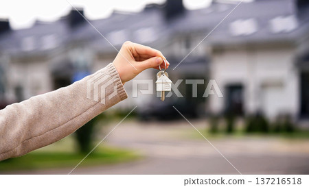 Woman Holds House Shaped Key, Buying Real Estate, Renting. Realtor Welcomes New Owner. Modern Townhouses In Background. Moving Day, Home Purchase, Fresh Start, Investment. 137216518
