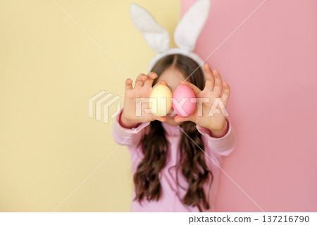 A girl with rabbit ears shows Easter eggs painted yellow and pink. A girl with rabbit ears shows Easter eggs painted yellow and pink. 137216790
