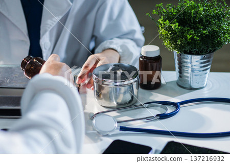 Medical team having a meeting with doctors in white lab coats and surgical scrubs seated at a table discussing a patients working online using computers in the medical industry. 137216932