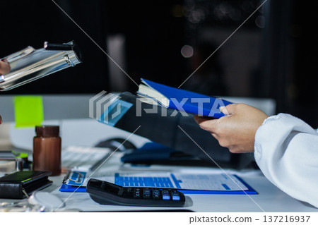 Medical team having a meeting with doctors in white lab coats and surgical scrubs seated at a table discussing a patients working online using computers in the medical industry. Medical team having a meeting with doctors in white lab coats and surgical scrubs seated at a table discussing a patients working online using computers in the medical industry. 137216937