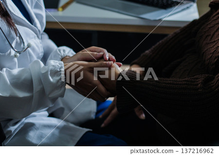 Senior patient lying in hospital bed receiving comforting touch from young female nurse, hands gently clasped together, medical care setting visible Senior patient lying in hospital bed receiving comforting touch from young female nurse, hands gently clasped together, medical care setting visible 137216962
