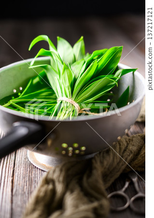 Fresh wild garlic leaves in metal colander on rustic wooden surface Fresh wild garlic leaves in metal colander on rustic wooden surface 137217121
