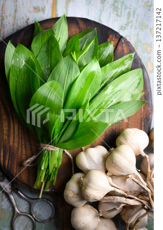 Wild garlic bundle placed on wooden board with kitchen scissors Wild garlic bundle placed on wooden board with kitchen scissors 137217142