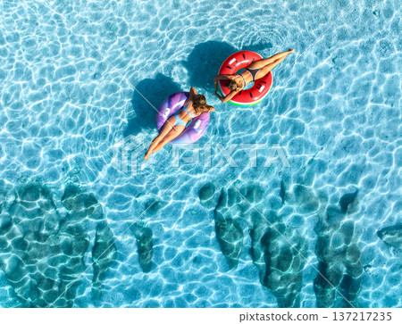 Aerial view of beautiful young women on swim rings in blue sea Aerial view of beautiful young women on swim rings in blue sea 137217235