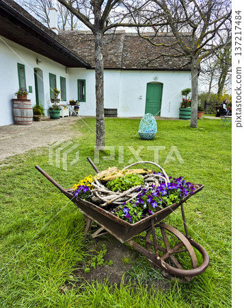 Rustic wheelbarrow garden planter with blooming pansies and easter egg structure in the background during the Easter holidays Rustic wheelbarrow garden planter with blooming pansies and easter egg structure in the background during the Easter holidays 137217484