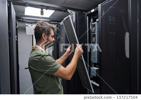 IT technician performing server maintenance in a data center rack replacing air filter panel 137217504