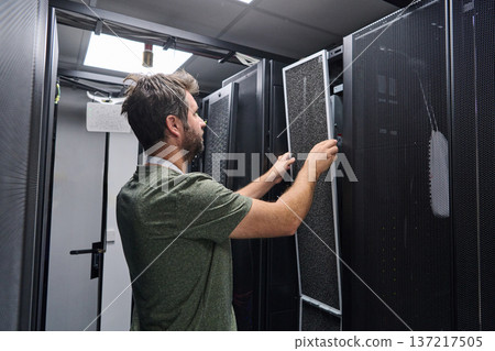 Data center technician replaces air filter in server rack during routine IT maintenance and hardware check Data center technician replaces air filter in server rack during routine IT maintenance and hardware check 137217505