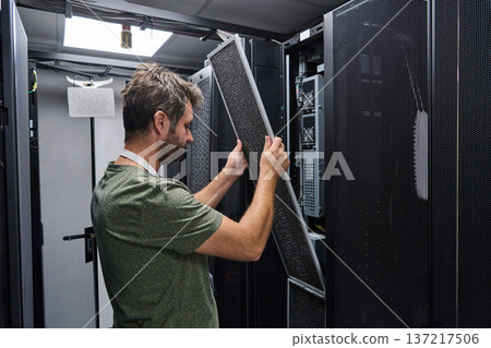 IT technician replacing air filter panel in a server room rack during data center maintenance and hardware service IT technician replacing air filter panel in a server room rack during data center maintenance and hardware service 137217506