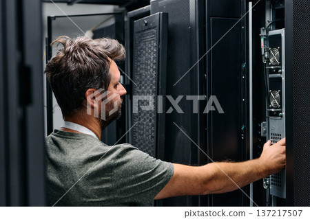 It technician checking servers in a data center rack performing hardware maintenance and network troubleshooting It technician checking servers in a data center rack performing hardware maintenance and network troubleshooting 137217507