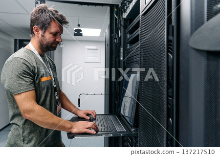 It technician configuring servers on a rack-mounted laptop in a modern data center server room It technician configuring servers on a rack-mounted laptop in a modern data center server room 137217510