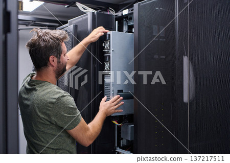 IT technician installing server hardware in a data center rack performing maintenance and configuration 137217511
