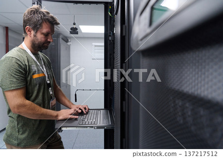 IT technician working on server rack with laptop in a modern data center server room 137217512