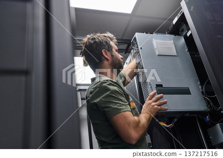 IT technician installing server hardware in a data center rack performing maintenance and network setup 137217516
