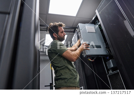 Data center technician installing server hardware and cabling in a server rack during maintenance work Data center technician installing server hardware and cabling in a server rack during maintenance work 137217517