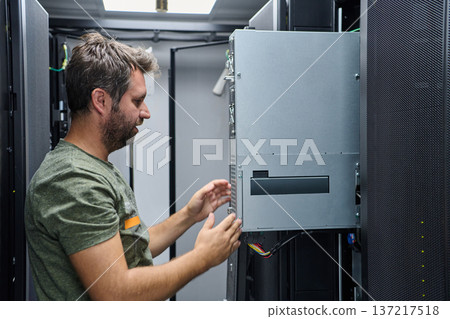 IT technician inspecting and installing server hardware inside a data center equipment rack IT technician inspecting and installing server hardware inside a data center equipment rack 137217518