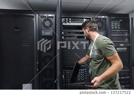 IT technician working on servers in a data center with laptop performing maintenance and monitoring IT technician working on servers in a data center with laptop performing maintenance and monitoring 137217522