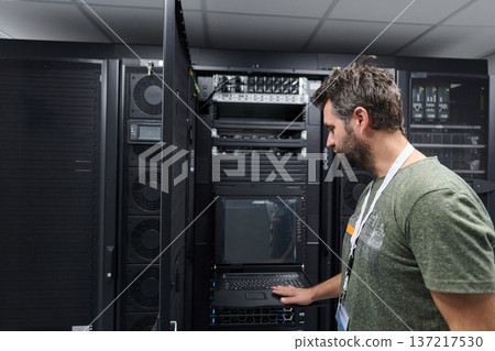 IT technician checking server rack console in a data center, focused on maintenance and monitoring 137217530