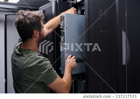 Data center technician installing server hardware in a rack cabinet during routine maintenance and upgrade Data center technician installing server hardware in a rack cabinet during routine maintenance and upgrade 137217533