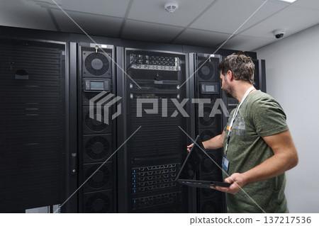 IT technician checking servers in a modern data center server room with laptop and racks IT technician checking servers in a modern data center server room with laptop and racks 137217536
