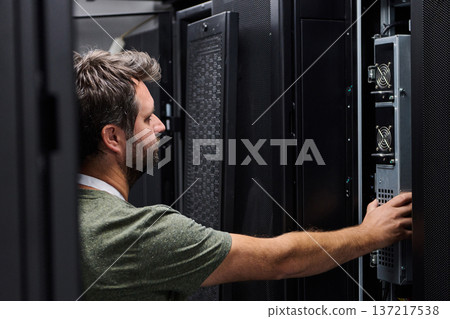 It technician inspecting servers in a data center server rack for maintenance and network support 137217538
