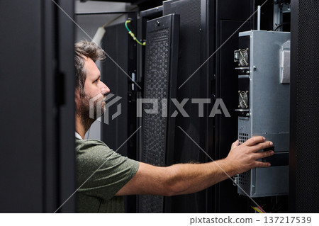 IT technician installing server hardware in a data center rack performing maintenance and inspection IT technician installing server hardware in a data center rack performing maintenance and inspection 137217539