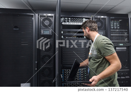 IT technician inspecting server rack in a data center with laptop during maintenance IT technician inspecting server rack in a data center with laptop during maintenance 137217540