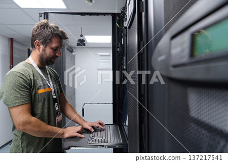 IT technician configuring servers on a rack console in a data center server room 137217541