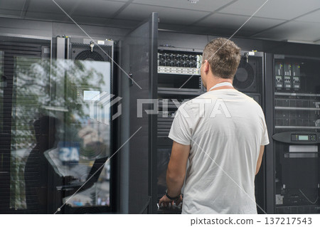 IT technician working on server rack in a modern data center checking network hardware and equipment 137217543