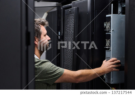 It technician performing server maintenance in a data center server rack with focused attention It technician performing server maintenance in a data center server rack with focused attention 137217544