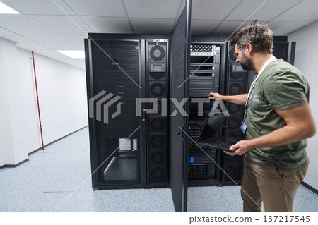 IT technician inspecting server racks with laptop in a secure data center server room IT technician inspecting server racks with laptop in a secure data center server room 137217545